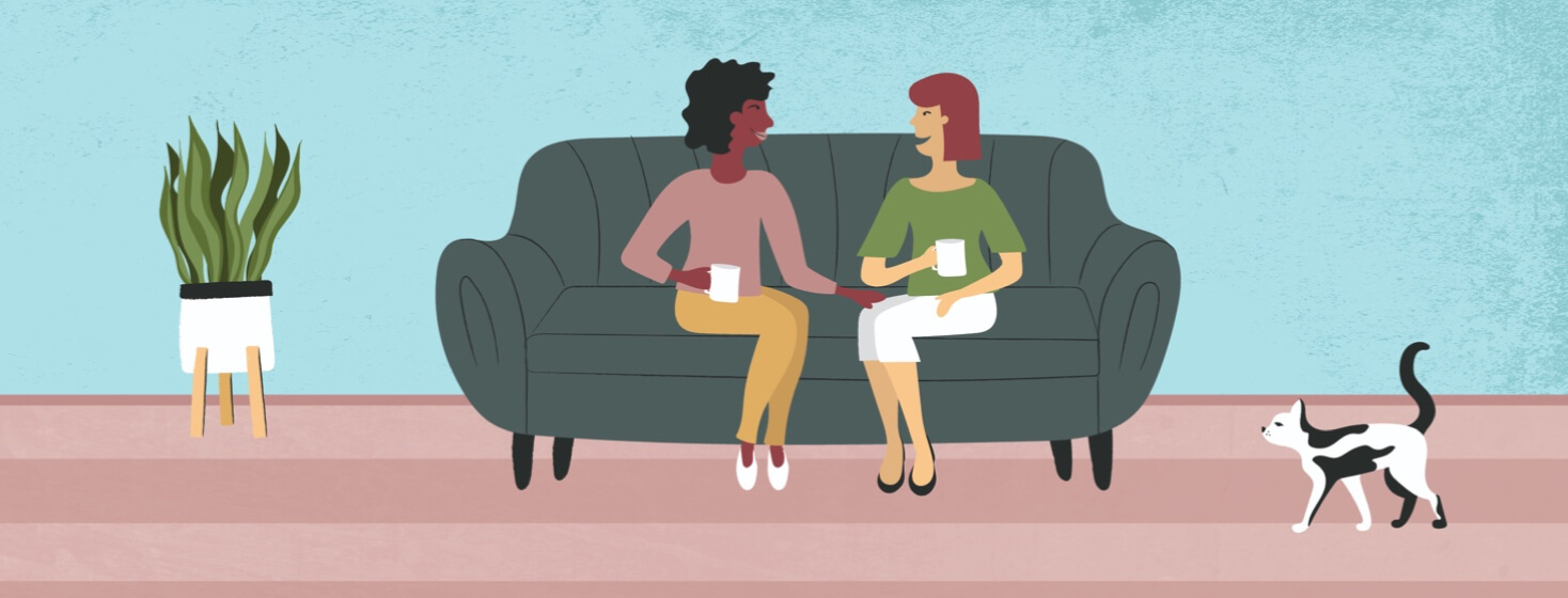 Two woman sitting on a couch talking and drinking tea