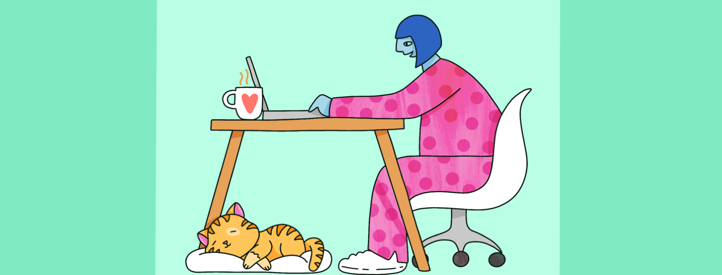 A woman sits at her desk in pajamas and works on her laptop at home with a cat at her feet