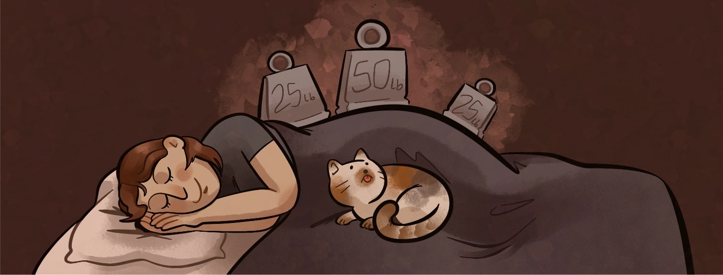 A woman is sleeping happily on her side, on top of her blanket are three different weights, her cat is laying with her and looking at the weights. Sleep, rest, cat, animal, pet, weighted